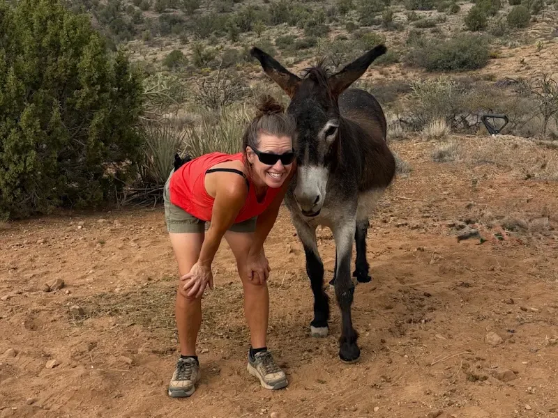 A caretaker smiling beside a donkey leaning in close