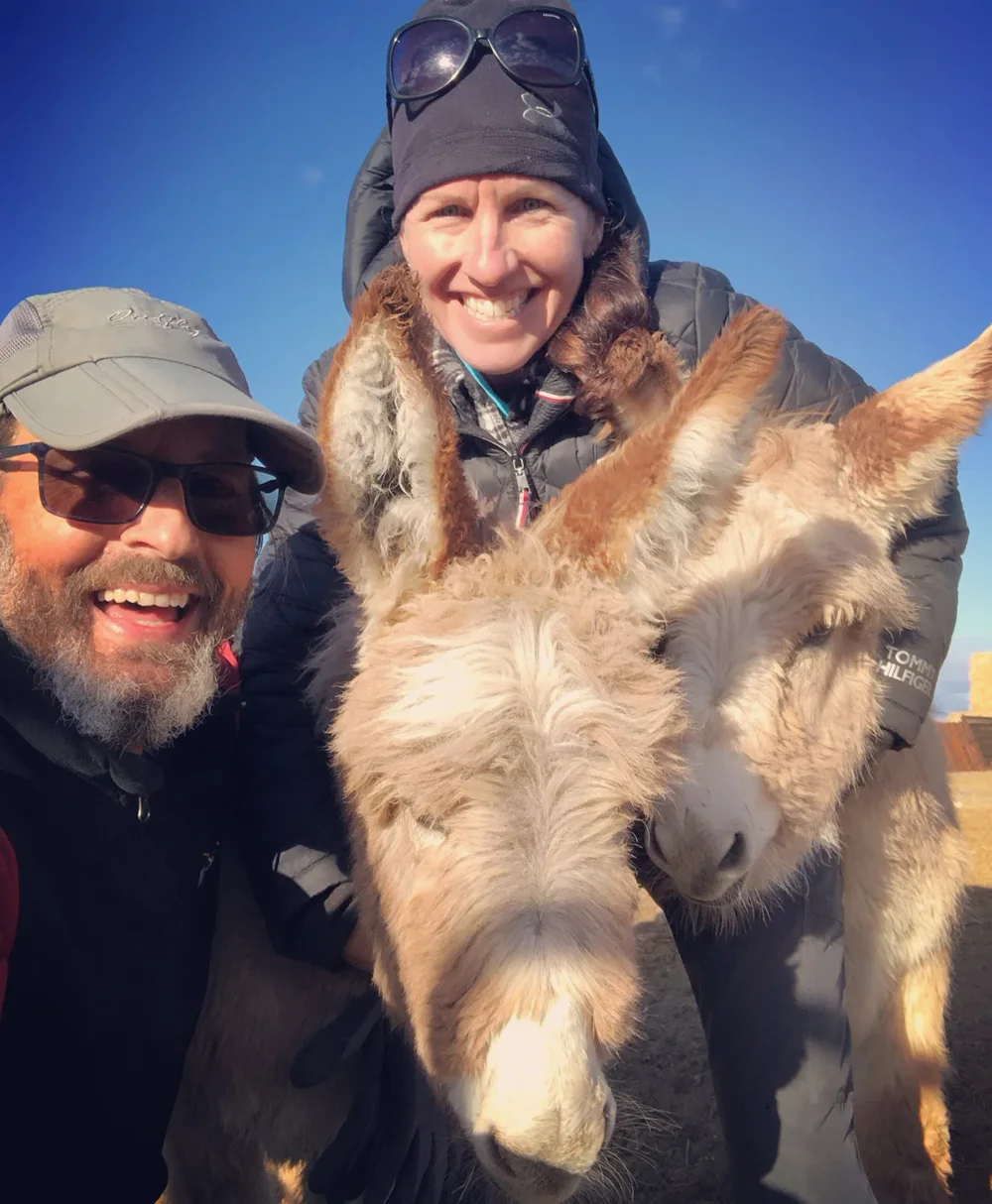 A smiling selfie with two fuzzy young burros at the rescue